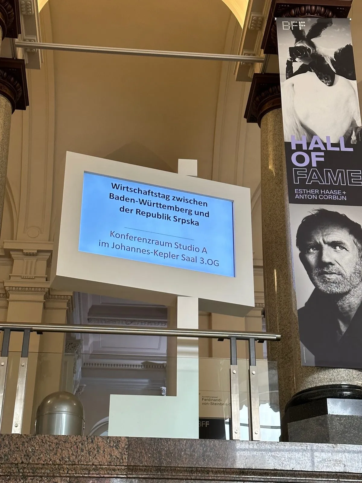 Hinweisschild im Treppenhaus des Haus der Wirtschaft: ein Bildschirm nennt den Wirtschaftstag zwischen Baden-Württemberg und der Republika Srpska und als Ort den Konferenzraum Studio A im Johannes-Kepler-Saal im dritten Obergeschoss.