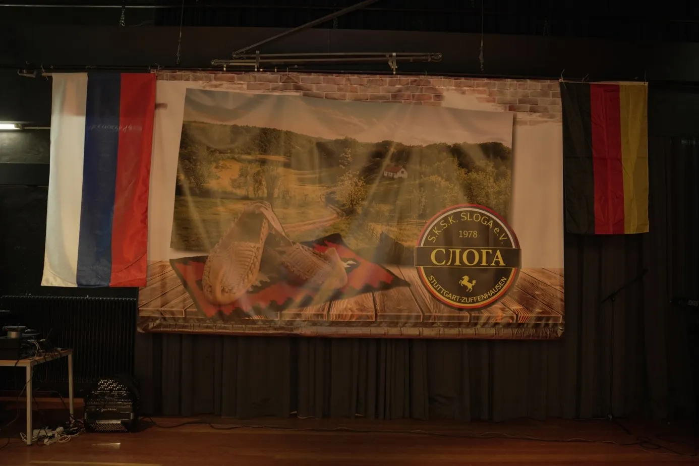 Die Bühne der Festhalle mit einem großen Banner des Vereins Sloga von 1978, links die Flagge der Republika Srpska, rechts die Flagge Deutschlands.