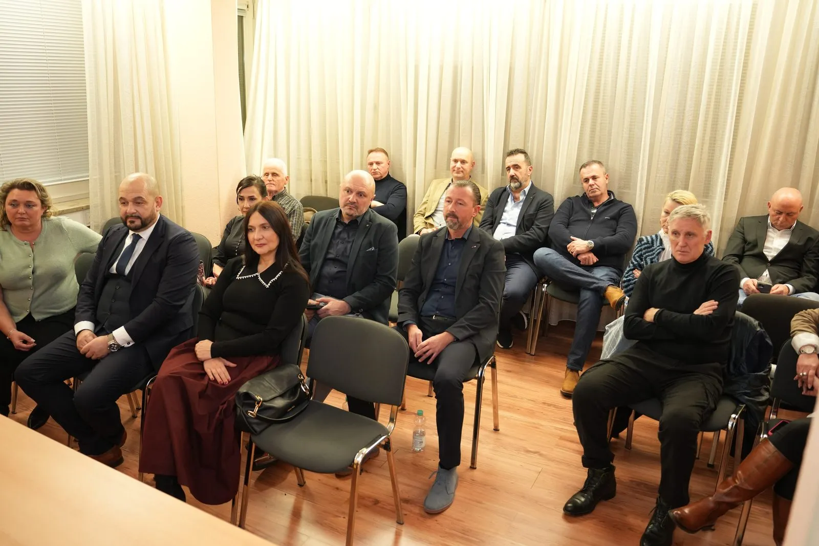 Rund zwanzig Gäste sitzen auf Stuhlreihen in einem hellen Raum mit Vorhängen und verfolgen die Diskussion.