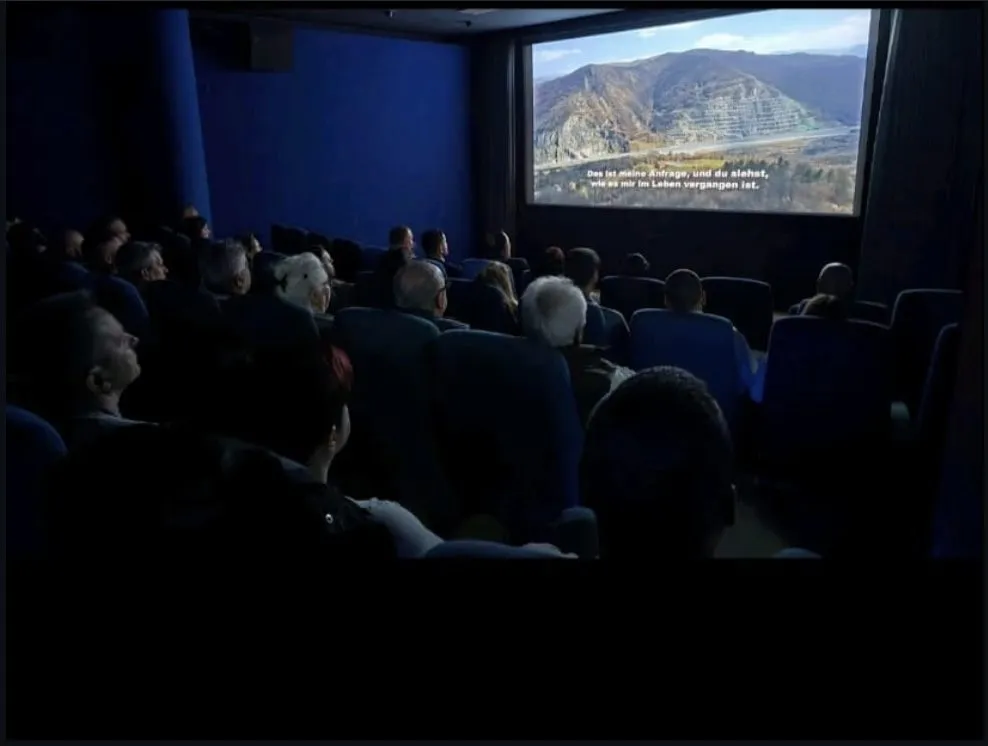 Abgedunkelter Saal während der Vorführung. Auf der Leinwand eine Berglandschaft mit deutschem Untertitel.