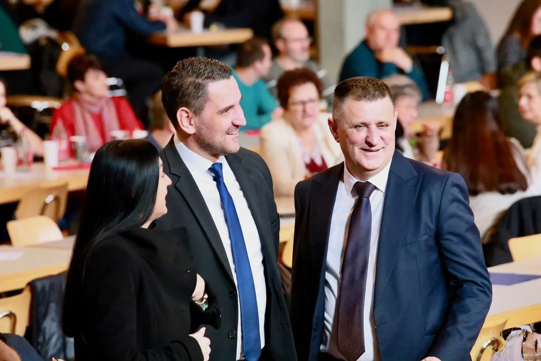 Drei Gäste stehen im Gespräch beieinander, im Hintergrund die besetzten Tischreihen des Saals.