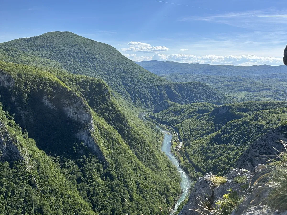 Blick von einem Felsvorsprung über eine bewaldete Schlucht, in der Tiefe windet sich ein türkisfarbener Fluss durch das Tal.