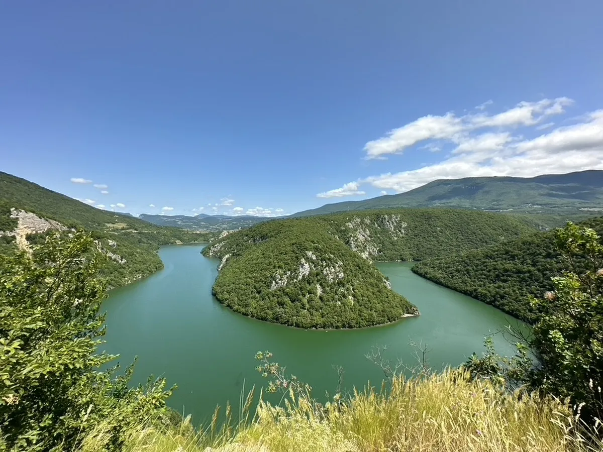 Ein türkisgrüner Stausee zwischen bewaldeten Hügeln, in der Mitte eine bewaldete Halbinsel.